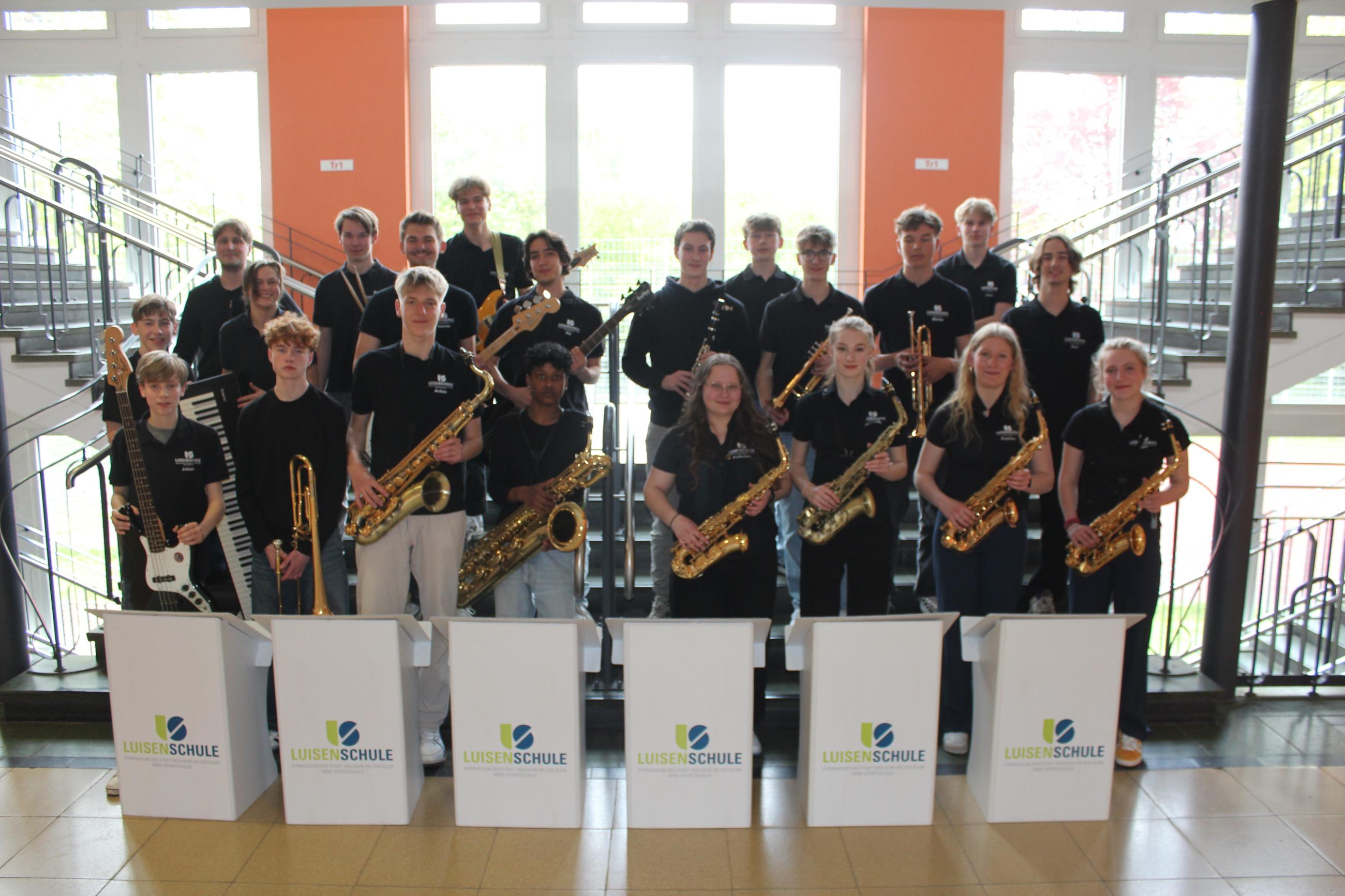 Das Foto zeigt die BigBand der Luisenschule in einem Treppenhaus. Die Schülerinnen und Schüler halten ihre Instrumente in den Händen.