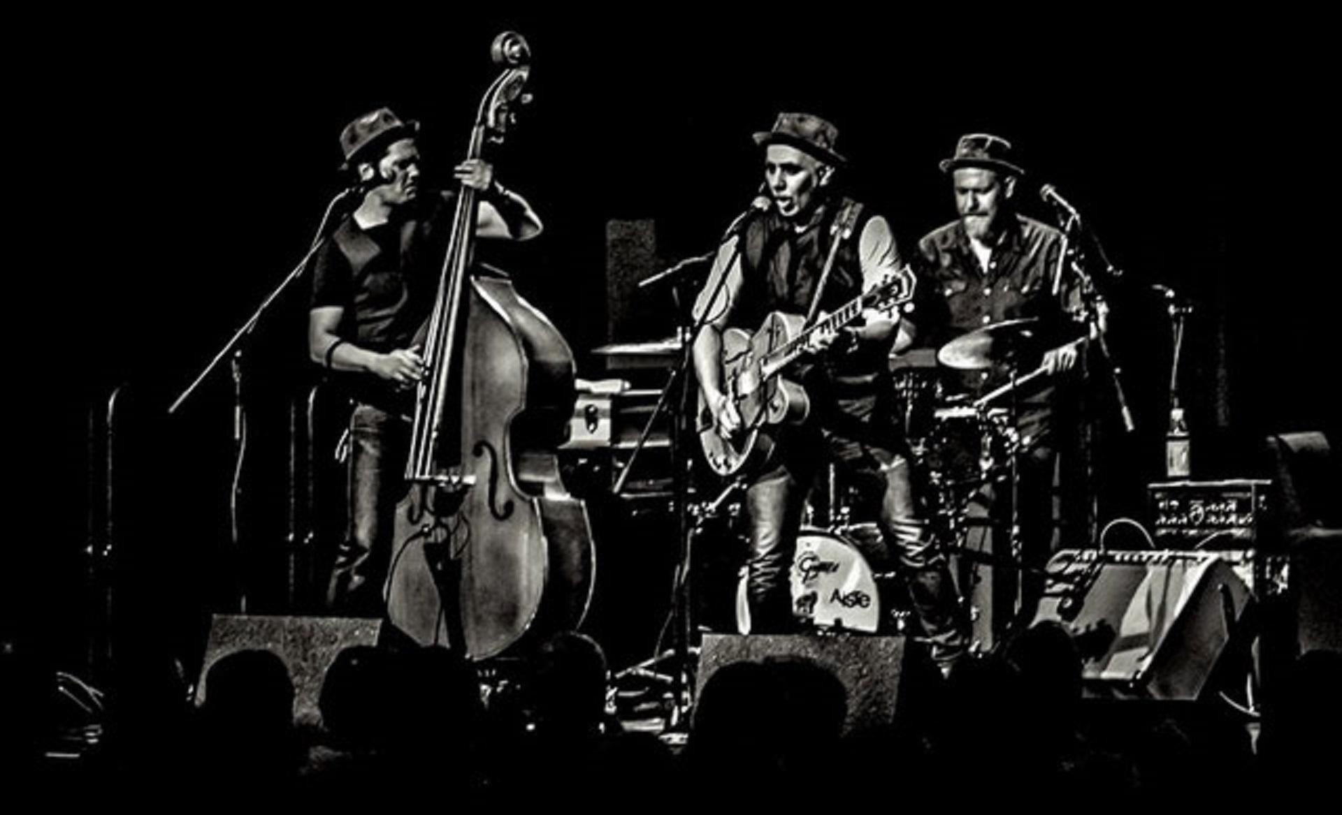 Das Bild zeigt die Band Adriano BaTolba Trio bei einem Bühnenauftritt. Es handelt sich um ein  Foto in schwarz-weiß.