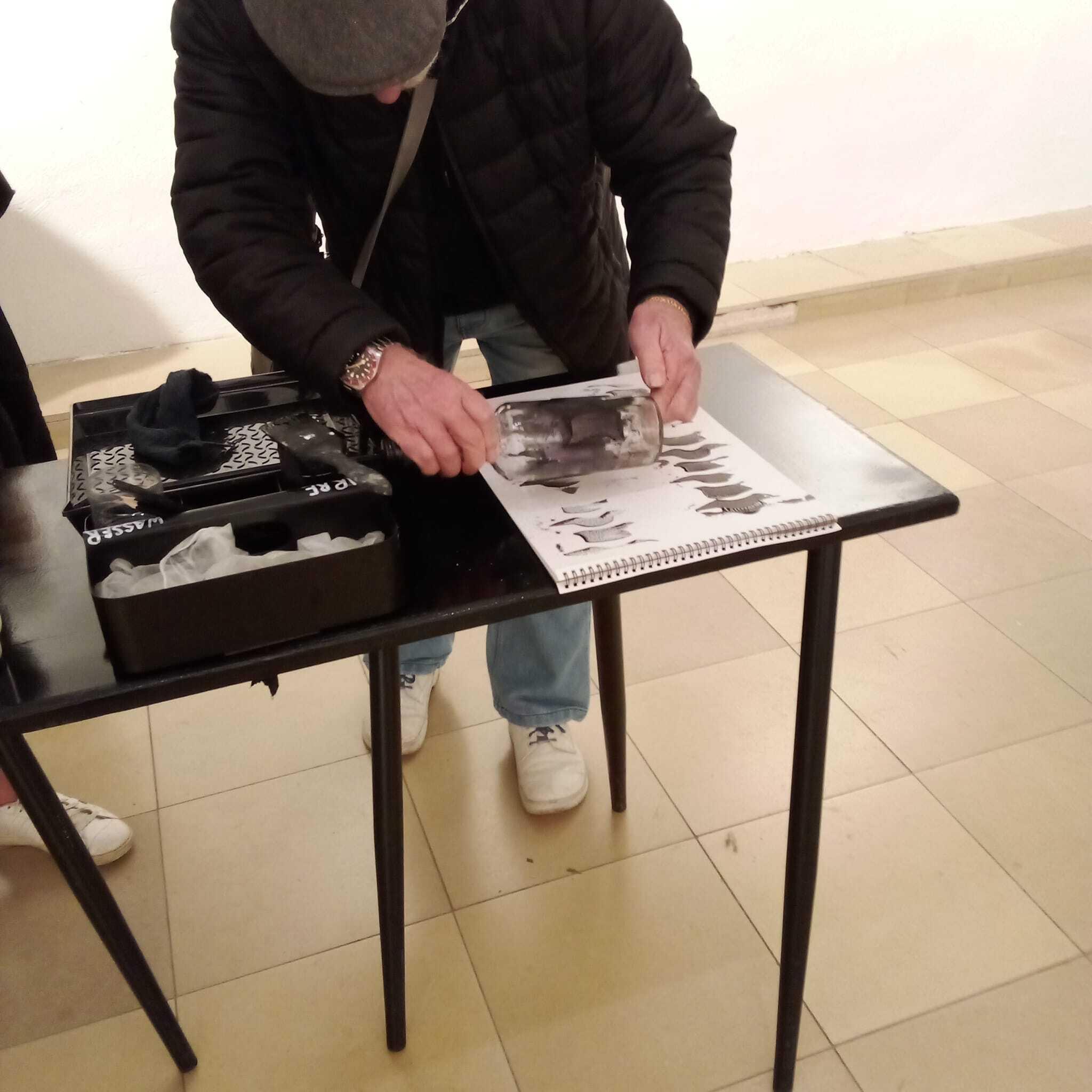 Das Foto zeigt die Aktion der Mülheimer Künstlerin Atti Mülders "Print yourself a spine". Ein Herr druckt mit einer Rollwalze seine Variante eines Rückgrats auf ein weißes Blatt Papier.
