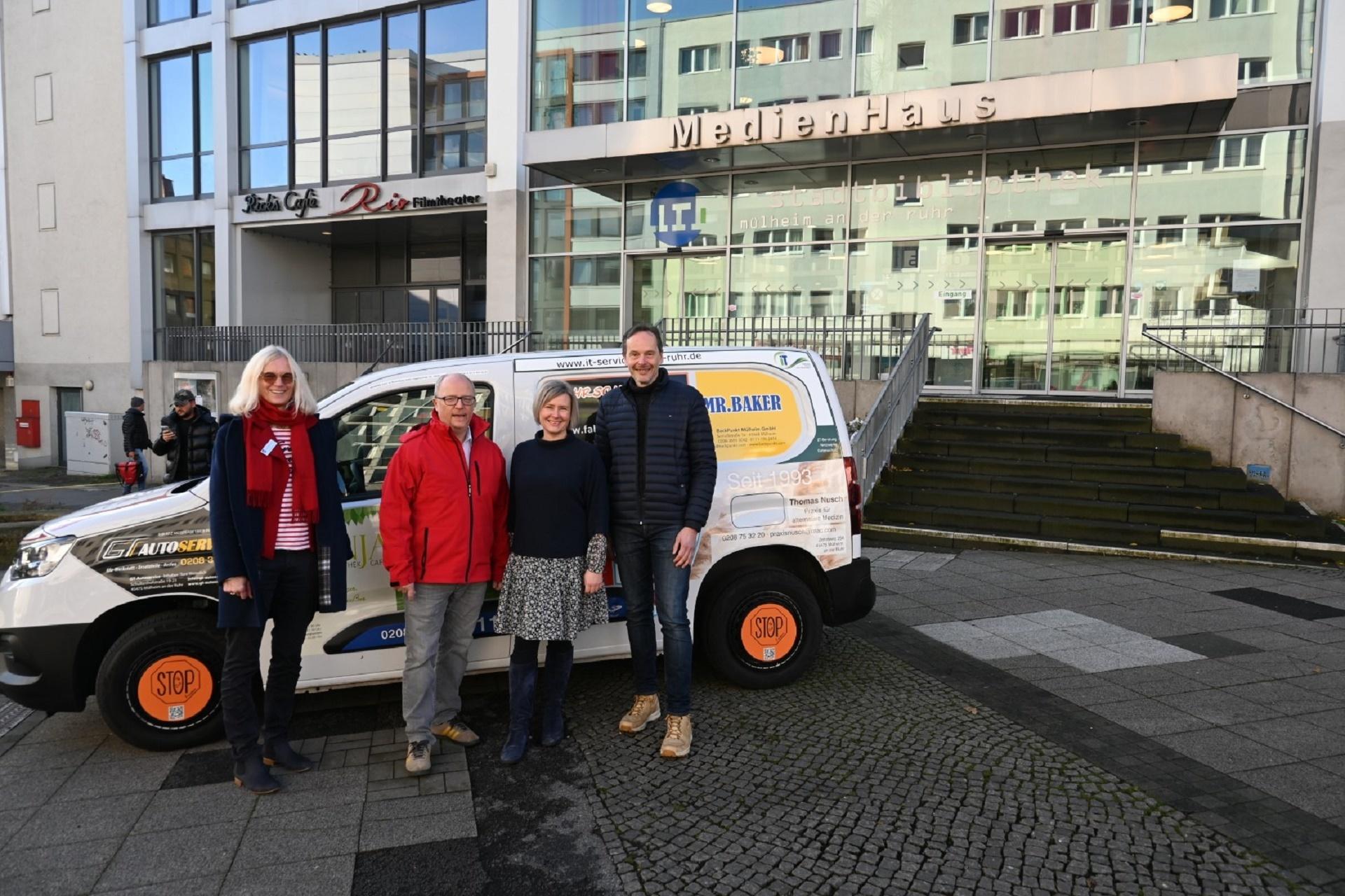 Das Bild zeigt das neue Fahrzeug der Stadtbibliothek mit drei von 20 Sponsoren vor dem MedienHaus.