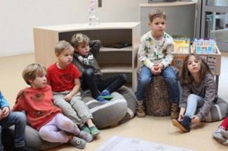 Kinder sitzen auf Kissen und hören zu.