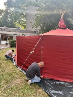 Das rote Erzählzelt wirf von zwei Helfern im Garten des Nachbarschaftshauses aufgebaut.