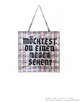 Eine große karierte Tragetasche mit schwarzer Altdeutscher Aufschrift "möchtest du einen N-Wort sehen?". Das N-Wort ist im Original ausgeschrieben aber auf der Abbildung zensiert dargestellt.