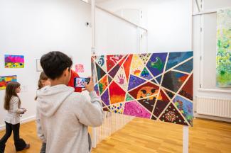 Ausstellungssituation. Ein Junge steht vor einem Kunstwerk und fotografiert es mit seinem Handy ab.