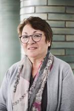 Das Bild zeigt ein Porträtfoto von Maria Thies, Mitarbeiterin im Kunstmuseums Mülheim an der Ruhr. Das Foto wurde im Museumsfoyer aufgenommen. Im Hintergrund sind die charakteristischen grün gekachelten Säulen erkennbar.