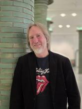 Ein lachender Mann steht an einer grünen Säule.