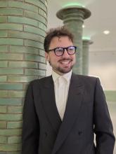 Ein lachender Mann steht an einer grünen Säule.
