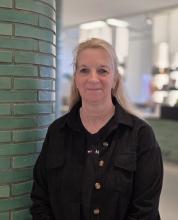 Eine lachende Frau steht an einer grünen Säule.
